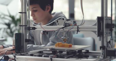Çocuk evde 3D baskı öğreniyor, ön planda profesyonel 3D yazıcı
