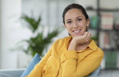 Huzurlu kadın evde poz veriyor, koltukta oturuyor ve kameraya bakıyor.