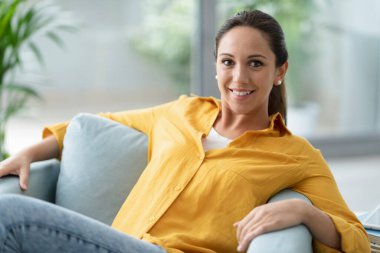 Huzurlu kadın evde poz veriyor, koltukta oturuyor ve kameraya bakıyor.