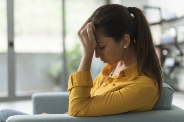 Depresyondaki genç kadın evdeki oturma odasında oturuyor. Umutsuz ve üzgün hissediyor.