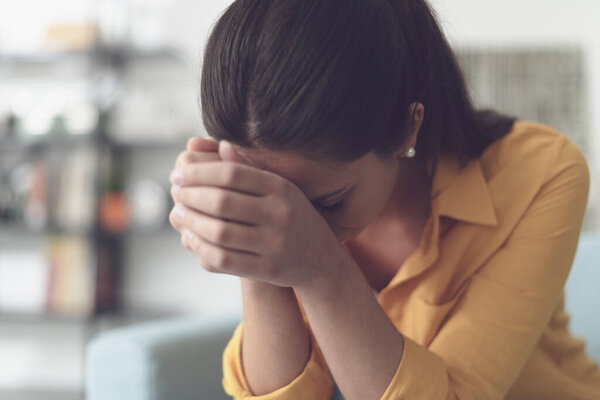 Depressed young woman sitting in the living room at home, she is feeling hopeless and sad