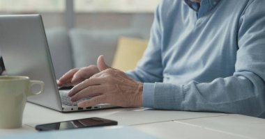 Masasında oturan ve laptopuyla bağlantı kuran kıdemli adam, eller yukarı.