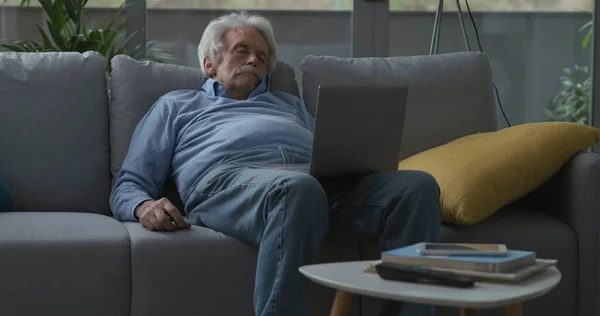 老年人一边在沙发上睡觉 一边看笔记本电脑上的视频 — 图库照片