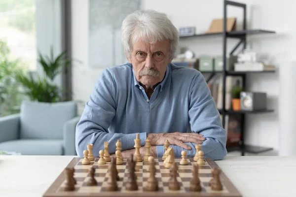 Уверенный Пожилой Человек Играет Дома Шахматы Смотрит Камеру — стоковое фото