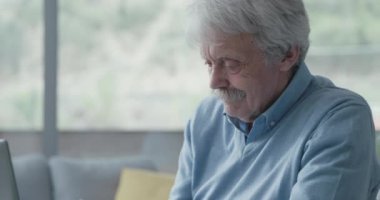 Üst düzey bir adam masada oturuyor ve bir dizüstü bilgisayar kullanıyor.