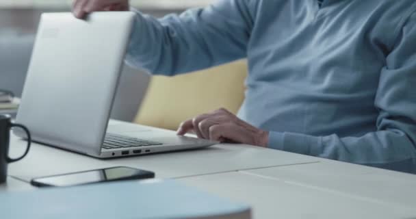 Senior man sitting at desk and using a laptop — Stock Video