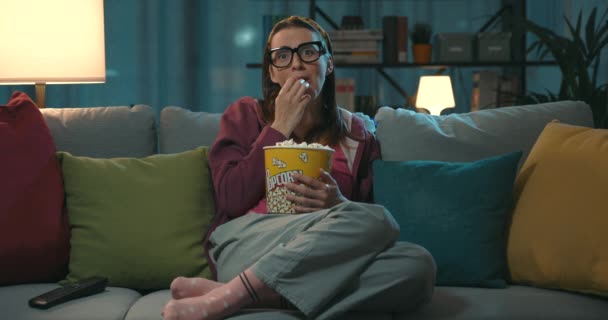 幸せな女性リラックスオンザソファと見て彼女のお気に入りのシリーズオンテレビ 彼女は食べているポップコーン — ストック動画