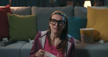 Televizyonda dram filmi izleyen duygusal bir kadın yerde oturup ağlıyor.