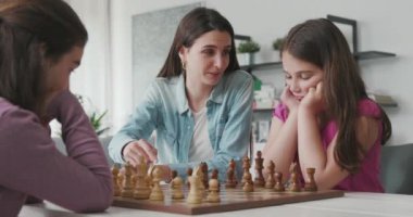 Young mother teaching chess to her daughters