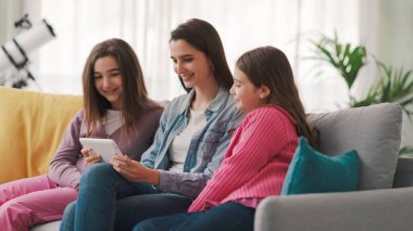 Happy girls sitting on the sofa and connecting with a digital tablet, they are watching movies online