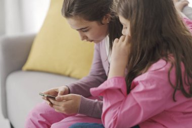 Cute young girls sitting on the sofa in the living room and using a smartphone together