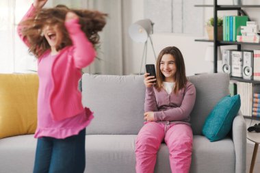 Happy girl shooting a video with her friend dancing in the living room