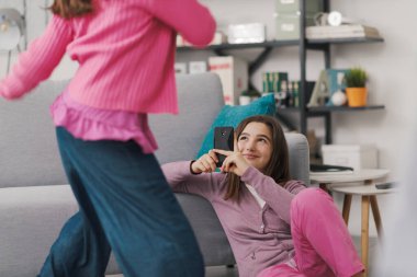Happy girl shooting a video with her friend dancing in the living room