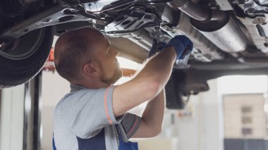 Araba altında çalışan profesyonel bir tamirci. Araç kontrolü yapıyor ve sızıntıları kontrol ediyor.