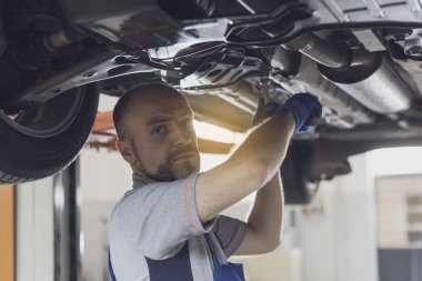 Araba altında çalışan profesyonel bir tamirci. Araç kontrolü yapıyor ve sızıntıları kontrol ediyor.
