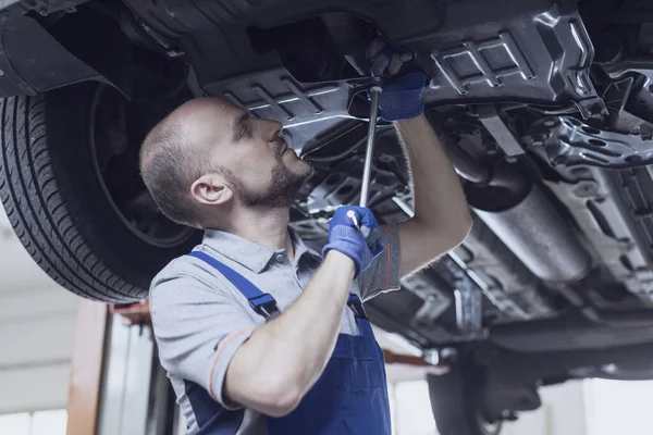 Araba altında çalışan profesyonel bir tamirci. Araç kontrolü yapıyor ve sızıntıları kontrol ediyor.