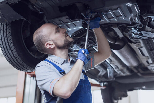Professional mechanic working under a car, he is doing a vehicle inspection and checking for leaks