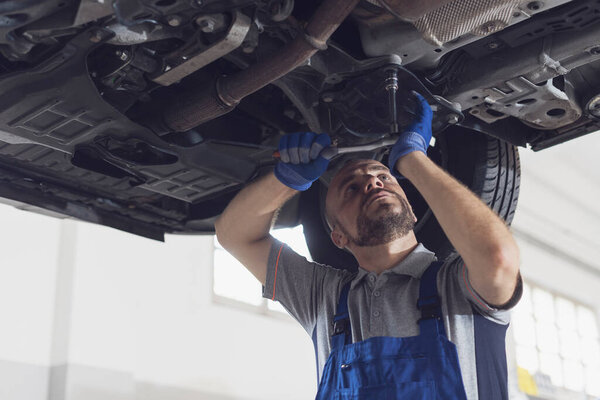 Professional mechanic working under a car, he is doing a vehicle inspection and checking for leaks