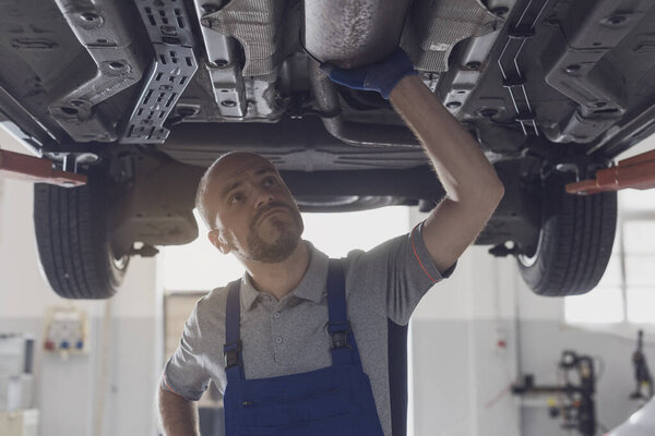 Professional mechanic working under a car in a repair shop, car maintenance and repair concept