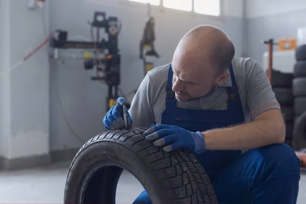 Mechanic checking tire tread depth and wear using a tire gauge, car maintenance concept