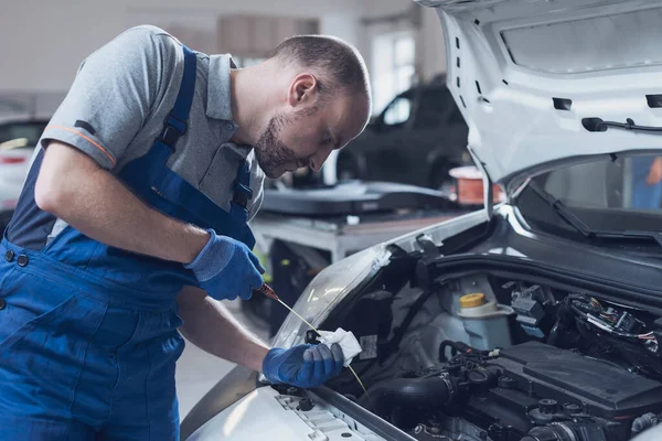 Tamirci araç teftişi yapıyor, arabanın yağ seviyesini ve kalitesini dipstick kullanarak kontrol ediyor.