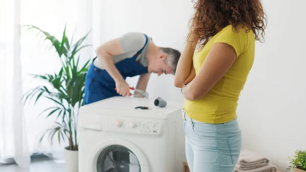 专业的管道工修理一台破洗衣机 客户正在看着他 修理服务理念 — 图库照片