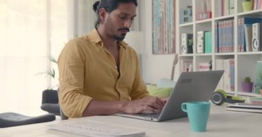 Hintli adam masada oturuyor ve laptopuyla evde çalışıyor.