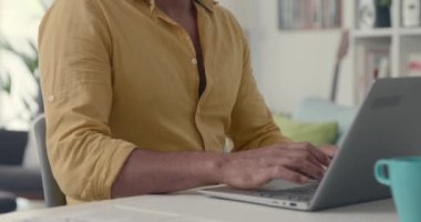 Adam masada oturuyor ve laptopuyla çalışıyor.