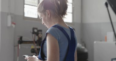 Araba tamir atölyesinde çalışan ve akıllı telefonlara bağlanan profesyonel kadın tamirci.