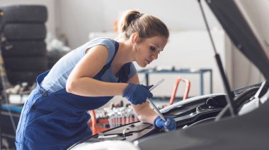 Araba tamir atölyesinde çalışan profesyonel kadın tamirci, bir araba motoru tamir ediyor.