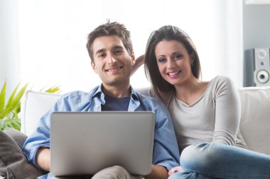 Couple relaxing on sofa with laptop clipart
