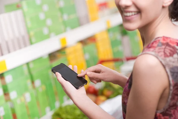 Mulher com celular no supermercado — Fotografia de Stock