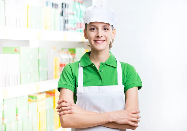 Smiling supermarket worker with shelf on background — Stock Photo, Image