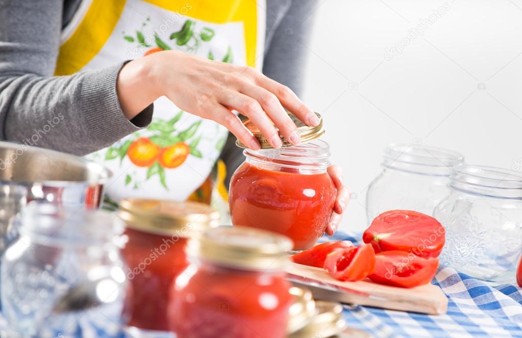 Woman filling glass jars with tomato sauce