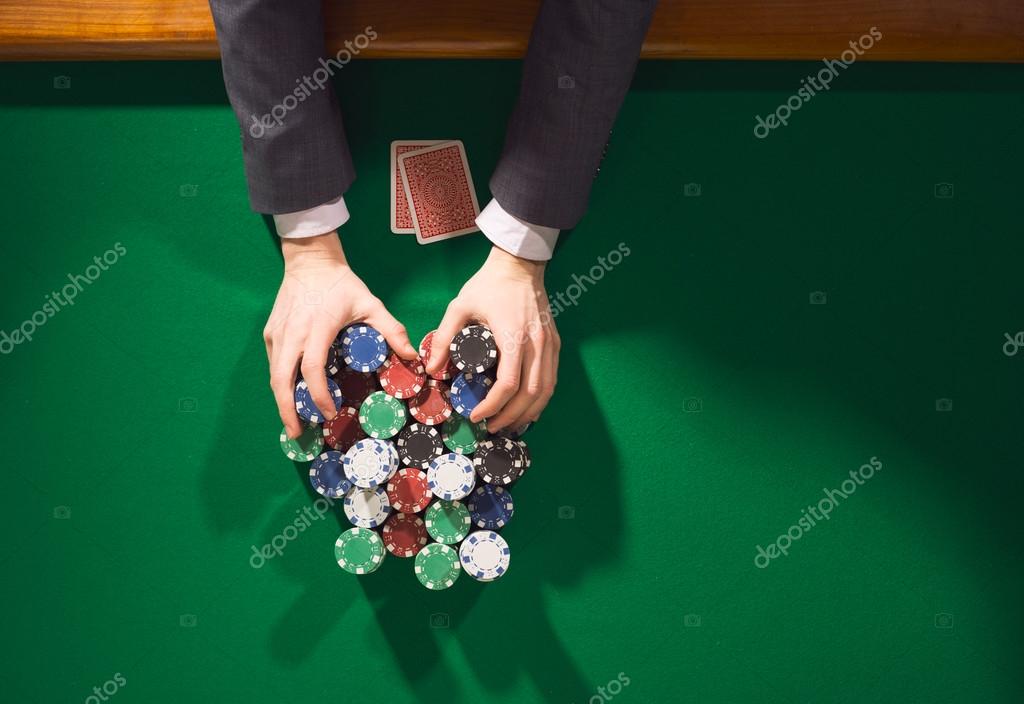 Poker player betting all in and holding a lot of chips stacks, hands close up, top view