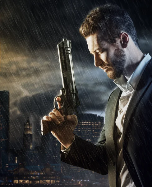 Agent under pouring rain holding a gun — Stockfoto