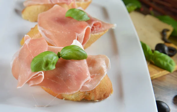 Bruschetta com prosciutto e folhas de manjericão — Fotografia de Stock