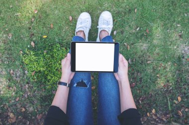 Açık havada otururken beyaz masaüstü ekranlı siyah tablet tableti tutan ve kullanan bir kadının en üstteki görüntüsü