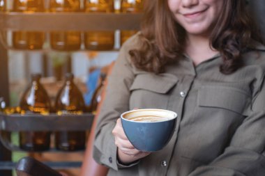 Kafede sıcak kahve içip kokan Asyalı bir kadının yakın plan görüntüsü.