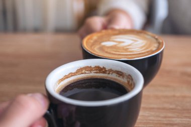 Kafe 'de iki kahve fincanını ahşap masaya tokuşturan bir adam ve bir kadının yakın görüntüsü.