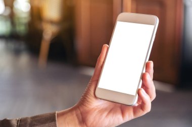 El ele tutuşmanın ve kafedeki bulanık arkaplan ile boş ekranlı beyaz bir cep telefonu görüntüsünün maketi