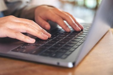 Masadaki dizüstü bilgisayarın klavyesini kullanan ve yazan ellerin yakın plan resmi