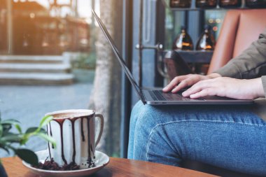 Kafede otururken dizüstü bilgisayarı kullanan ve daktilo kullanan bir kadının yakın plan resmi