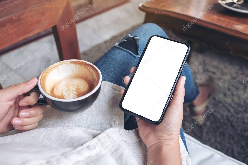 Mockup image of hands holding black mobile phone with blank white screen while drinking coffee 