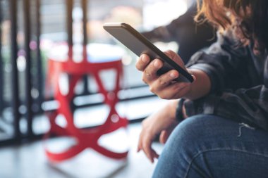 Kafede elinde tutan, kullanan ve akıllı telefona bakan bir kadının yakın plan görüntüsü.