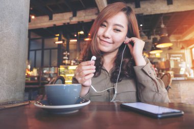 Kafede cep telefonuyla müzik dinleyen Asyalı güzel bir kadının yakın plan görüntüsü.