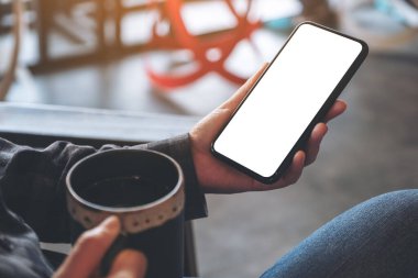 Kafede kahve içerken siyah cep telefonunu boş ekran ile tutan bir elin görüntüsü.