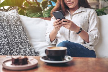 Kafedeki akıllı telefonu tutan, kullanan ve ona bakan güzel bir kadının yakın plan görüntüsü.