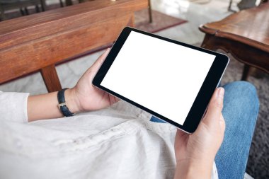 Kafede otururken siyah tableti beyaz ekranla tutan bir kadının ellerinin görüntüsü.