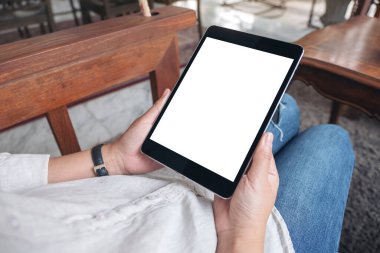 Kafede otururken siyah tableti beyaz ekranla tutan bir kadının ellerinin görüntüsü.